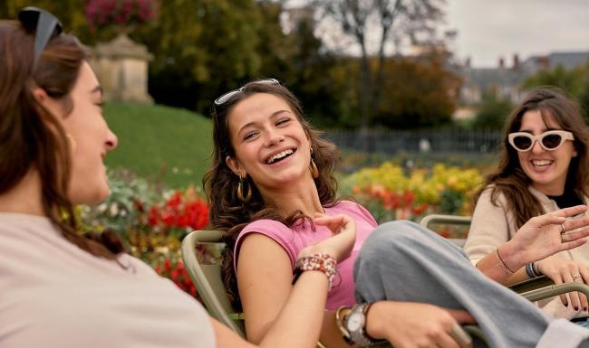 Three women sitting in chairs next to a garden and laughing.